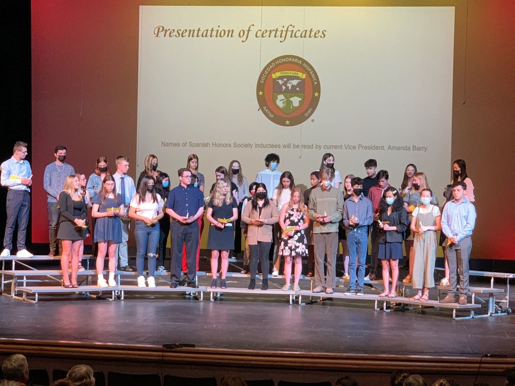 students on a stage with a large certificate in the background for Spanish Honors Society